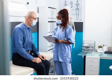 Female healthcare worker prepares caucasian old man for his medical appointment taking notes on clipboard. Male pensioner patient sharing his health background with african american nurse at clinic. - Powered by Shutterstock