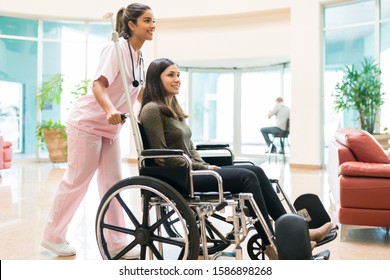 Female healthcare worker pushing recovered woman on wheelchair in hospital lobby - Powered by Shutterstock