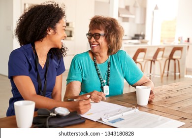 Female healthcare worker sitting at table smiling with a senior woman during a home health visit - Powered by Shutterstock