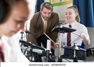 Female High School Student Playing Drums During A Music Class With A Teacher Watching Her.