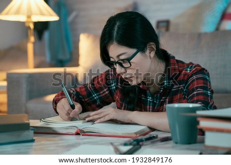 female high school student is transcribing math formula from textbook with attentive look. closeup of asian girl preparing for upcoming exam with full attention.