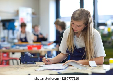 Female high school student writing notes at workbench in workshop