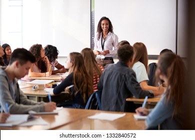 Female High School Teacher Standing In Front Of Interactive Whiteboard Teaching Lesson