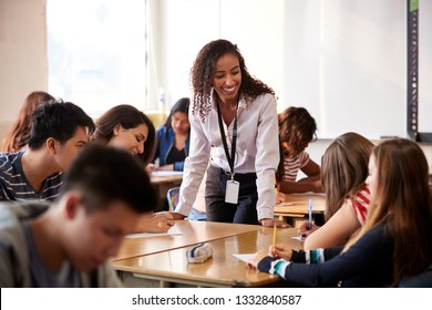 Female High School Teacher Standing By Student Table Teaching Lesson