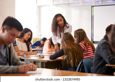 Female High School Teacher Standing By Student Table Teaching Lesson