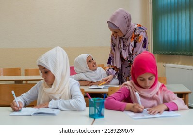 Female Hijab Muslim Teacher Helps School Children To Finish The Lesson In The Classroom.	