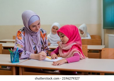 Female hijab Muslim teacher helps student girl to finish the lesson durind the school class in the classroom.	 - Shutterstock ID 2196279327
