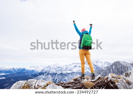 Female hiker with backpack raised her hands celebrating successful climb to top of mountain