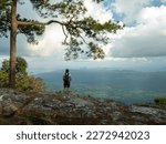 Female hiker with a backpack standing and enjoying the view During an adventurous journey exploring nature in the midst of abundant forest nature Rocky cliff area can see the landscape far and wide