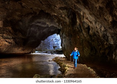 Female Hiker In Blue Wind Jacket Explore Karst Cave.