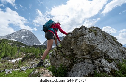 Female hiker climbing a rocky outcrop with a mountain peak in the background under a cloudy sky at the alps - Powered by Shutterstock