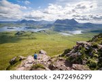A female hiker descending Stac Pollaidh with views of Suilven, Cul Mor and Loch Sionasgaig  in the distance in the Scottish Highlands on a sunny summers day in the UK