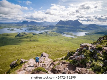 A female hiker descending Stac Pollaidh with views of Suilven, Cul Mor and Loch Sionasgaig  in the distance in the Scottish Highlands on a sunny summers day in the UK - Powered by Shutterstock