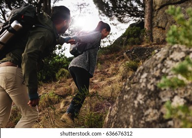 Female hiker helping her boyfriend uphill in the countryside. Young couple hiking in mountain.