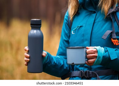 Female Hiker Holding Thermos With Hot Drink And Travel Mug In Forest. Woman Hiking And Camping Outdoors