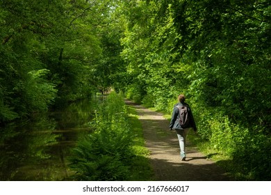 A female hiker on a footpath next to a canal in the Welsh countryside. lush green verdant trees grow in abundance in the pleasant natural surroundings of the Brecon and Monmouth canal - Shutterstock ID 2167666017