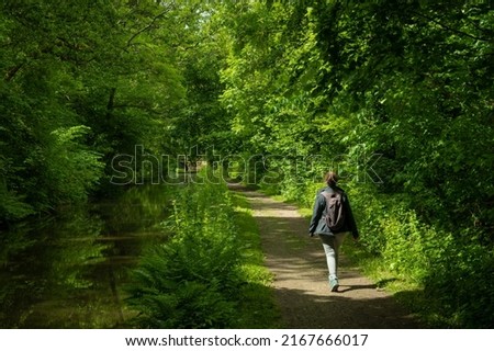 A female hiker on a footpath next to a canal in the Welsh countryside. lush green verdant trees grow in abundance in the pleasant natural surroundings of the Brecon and Monmouth canal