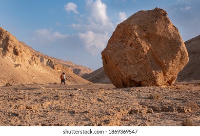 Female Hiker On A Trail In A Dry Wadi Hatira, Negev Desert, Israel. Desert Landscape With A Huge Boulder On A Hiking Trail.