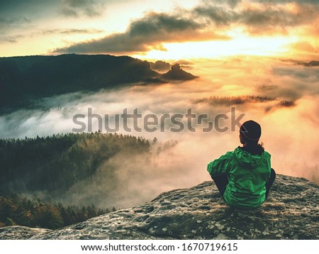 Female hiker takes a break and enjoys mountain views.  Female hiker backpacker sitting on the peak edge and enjoying mountains view valley during heavy mist