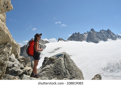 A female hiker takes in the view of high mountains and glaciers amid granite boulders on a beautiful clear day