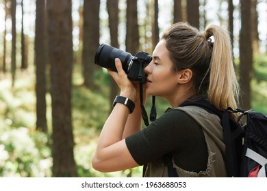 Female hiker taking photos using modern mirrorless camera in green forest