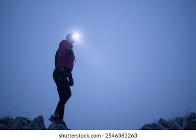 female Hiker or triathlon trail runner with a headlamp on a trail in the mountain with fog at night - Powered by Shutterstock