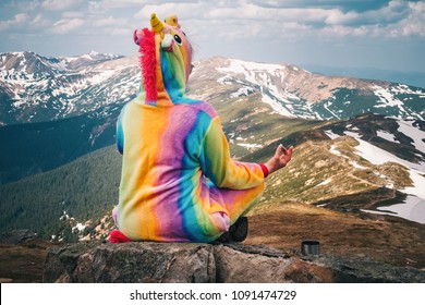 Female hiker in a unicorn suit meditating on top of the mountain on a Carpathian landscape background on a Spring day. Wanderlust travel concept.