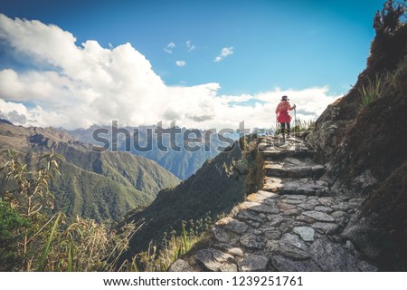 A female hiker is walking on the famous Inca trail of Peru with walking sticks. She is on the way to Machu Picchu.