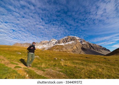 Female Hiker Walking On Footpath In A Colorful Valley With Scenic Sky And Clouds. Wide Angle Shot From Below In The Italian French Alps. Concept Of Healthy Lifestyle.