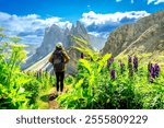 Female hiker walking on a path surrounded by flowers, enjoying the view of the odle mountains in the italian dolomites