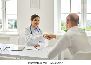 Female Hispanic Doctor Smiling Shaking Hands With A Senior Man Patient At Medical Clinic Office.