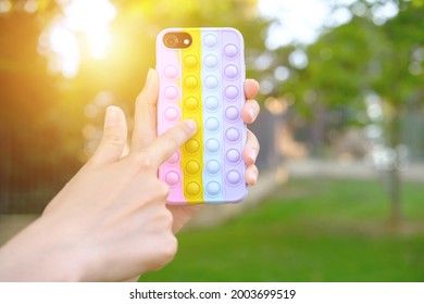 Female holding bright pop it bauble smartphone case infront of green garden. Antistress silicone toy. Simple dimple. Fidget gadget. Autism awareness. Stress reliever