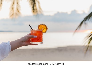 Female holding glass of cocktail on the beach at sunset - Shutterstock ID 2177507411
