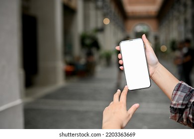 A Female Holding A Mobile Phone Over Blurred Community Mall In The Background. Smartphone White Screen Mockup, Close-up Image