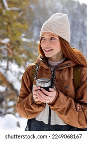 female holding mug of tea. redhead lady drink from thermo mug of coffee in nature. Warm up in frozen winter forest, warm hands. travel, wanderlust, Winter hike. Outdoor recreation on frosty day. - Shutterstock ID 2249068167