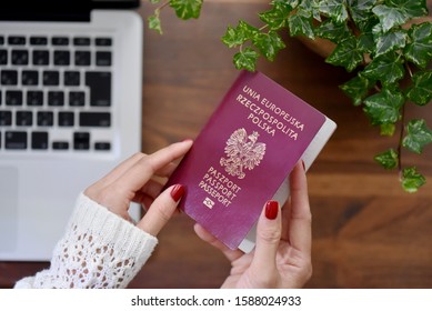 Female holding a Polish passport at office. Opened laptop computer on the wooden desk. Translation on the  passport text : 