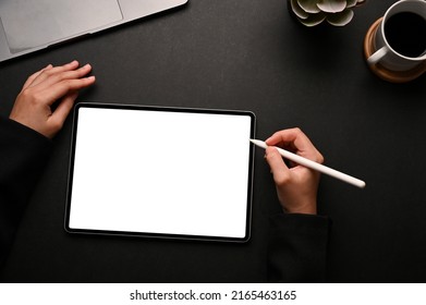A female holding a stylus pen and drawing on digital tablet touchpad white screen mockup on her modern black office workspace. top view