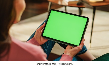 Female Holding Tablet Computer with Green Screen Mock Up Display. Woman Relaxing at Home, Watching Videos and Reading Social Media Posts on Mobile Device. Close Up Over the Shoulder Photo. - Powered by Shutterstock