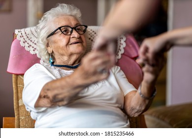 Female home carer supporting old woman to stand up from the armchair at care home - Shutterstock ID 1815235466