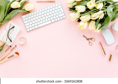 Female Home Office Desk. Workspace With Computer, Yellow Tulip Flowers, Stationery, Accessories On Pink Background.  Flat Lay, Top View.