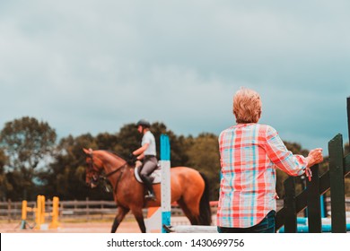 Female Horse Trainer Observing Young Rider On Jump Course