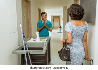 Female Hotel Guest Meets A Janitor With A Greeting Gesture Pushing A Cart Filled With Cleaning Supplies