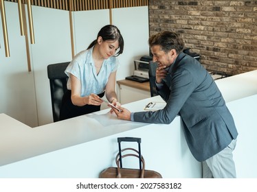 Female Hotel Receptionist Assisting Businessman For Checking In At Hotel On Tablet.
 Smiling Female Concierge Standing At Hotel Reception  And Showing Available Rooms On Digital Tablet To Guest.