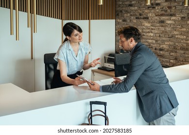 Female Hotel Receptionist Assisting Businessman For Checking In At Hotel On Tablet.
 Smiling Female Concierge Standing At Hotel Reception  And Showing Available Rooms On Digital Tablet To Guest.