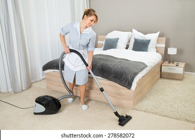 Female Housekeeper Cleaning Rug With Vacuum Cleaner In Hotel Room