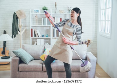 female housekeeper wearing apron dancing with mop while doing housework. young asian wife playing singing doing house chores in the living room enjoy the music. happy woman having fun at home. - Powered by Shutterstock