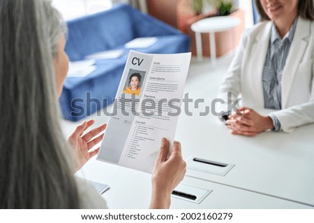 Female hr manager holding cv at job interview at desk, over shoulder view. Employer checking reading resume, curriculum vitae application. Human resources, hiring, recruitment and employment concept.