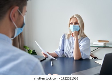 Female Hr Specialist Manager, Employer Wearing Face Mask Holding Cv Listening Male Candidate At Job Interview Meeting. Hiring And Employment During Covid Social Distance Safety Concept.