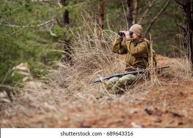 female hunter with binoculars ready to hunt, holding gun and walking in forest. 