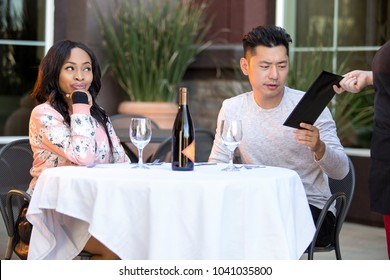 Female Hustler On A Date With A Gullible Man Paying For Her Restaurant Bill In An Outdoor Cafe.  The Image Depicts Gentleman Or Foolish Generosity In A Dating Scenario.